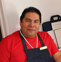 Photo of Duane Maktima wearing a red shirt and metalsmithing apron