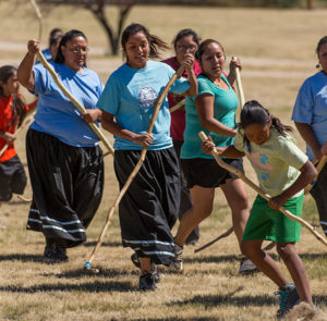 Indigenous women and girls playing a stick game on yellowed fall grass