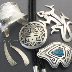 Grouping of sterling silver jewelry on a grey background showing hammer textured cuff and earrings, an overlay medallion bolo tie, pierced silver lizard pin, and an overlay stylized bear buckle set in the center with a turquoise cabochon by Duane Maktima..