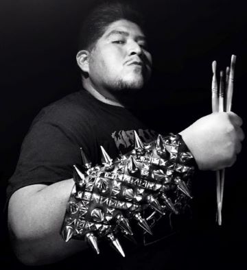 Black and white photo of Dwayne Manuel wearing a fore arm cover with spikes and holing paint brushes with his hand