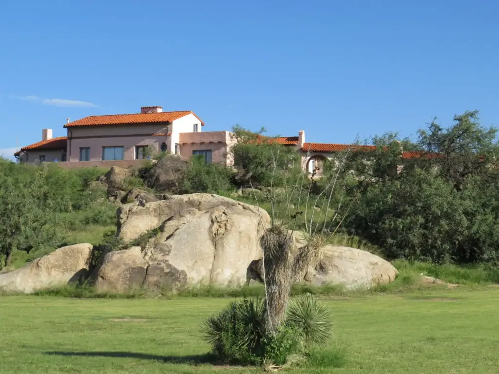 Amerind Museum on the horizon as it sits on higher rocky ground above a broad open space currently verdant green with a lone yucca plant in the middle.